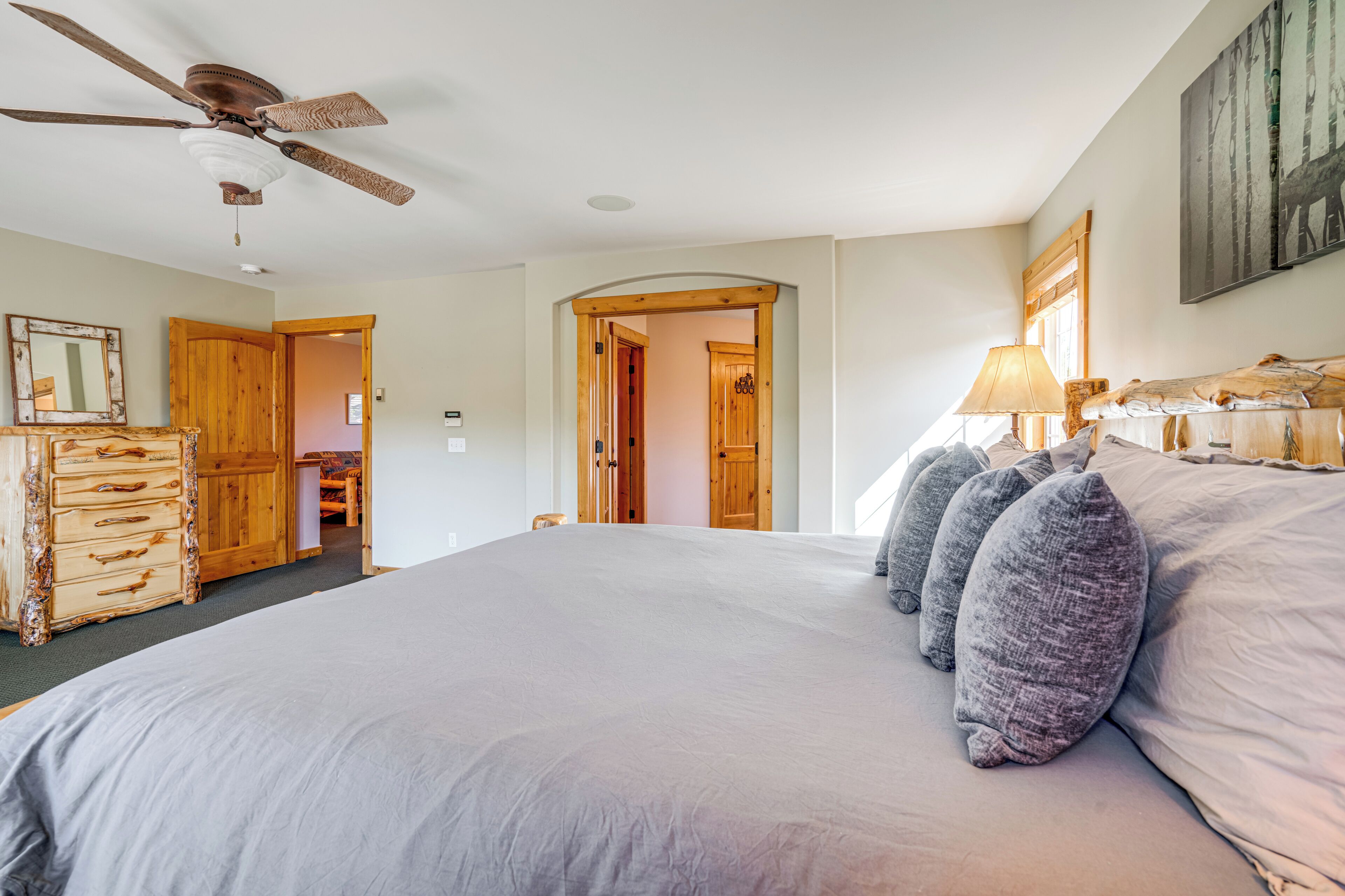 A bedroom with a large bed, wooden wardrobe, ceiling fan, and a door leading to another room.