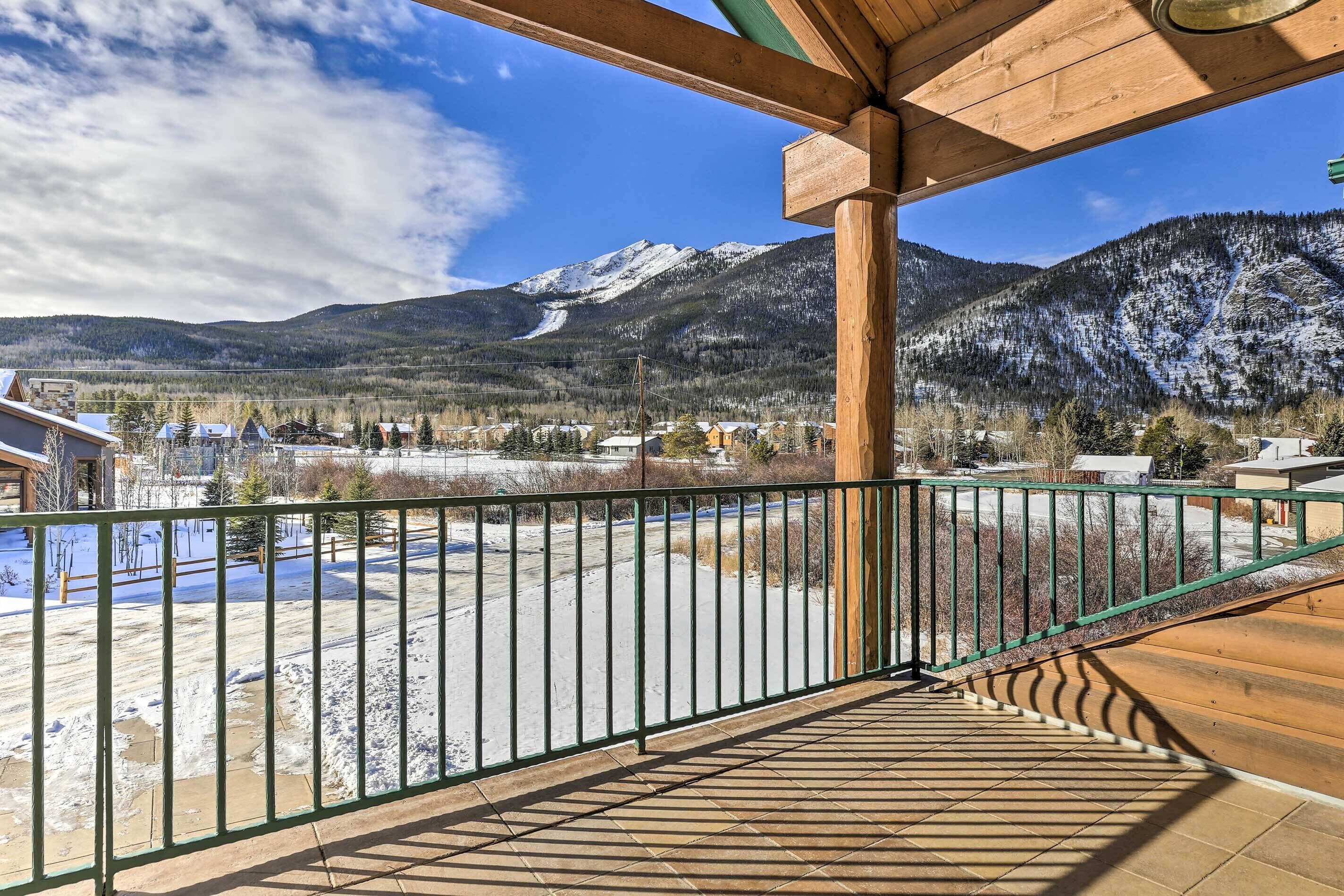 A wooden deck with a metal railing overlooking a snowy landscape with mountains in the background.