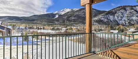 A wooden deck with a metal railing overlooking a snowy landscape with mountains in the background.
