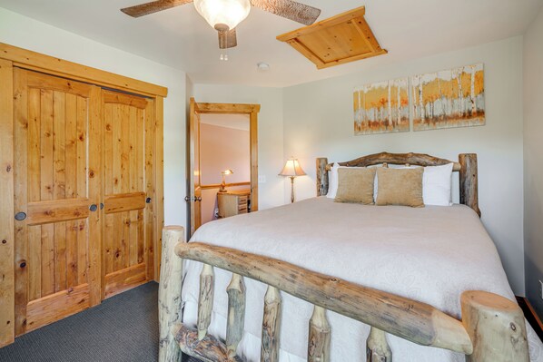 A bedroom with a wooden bed frame, a large mirror, and a ceiling fan.