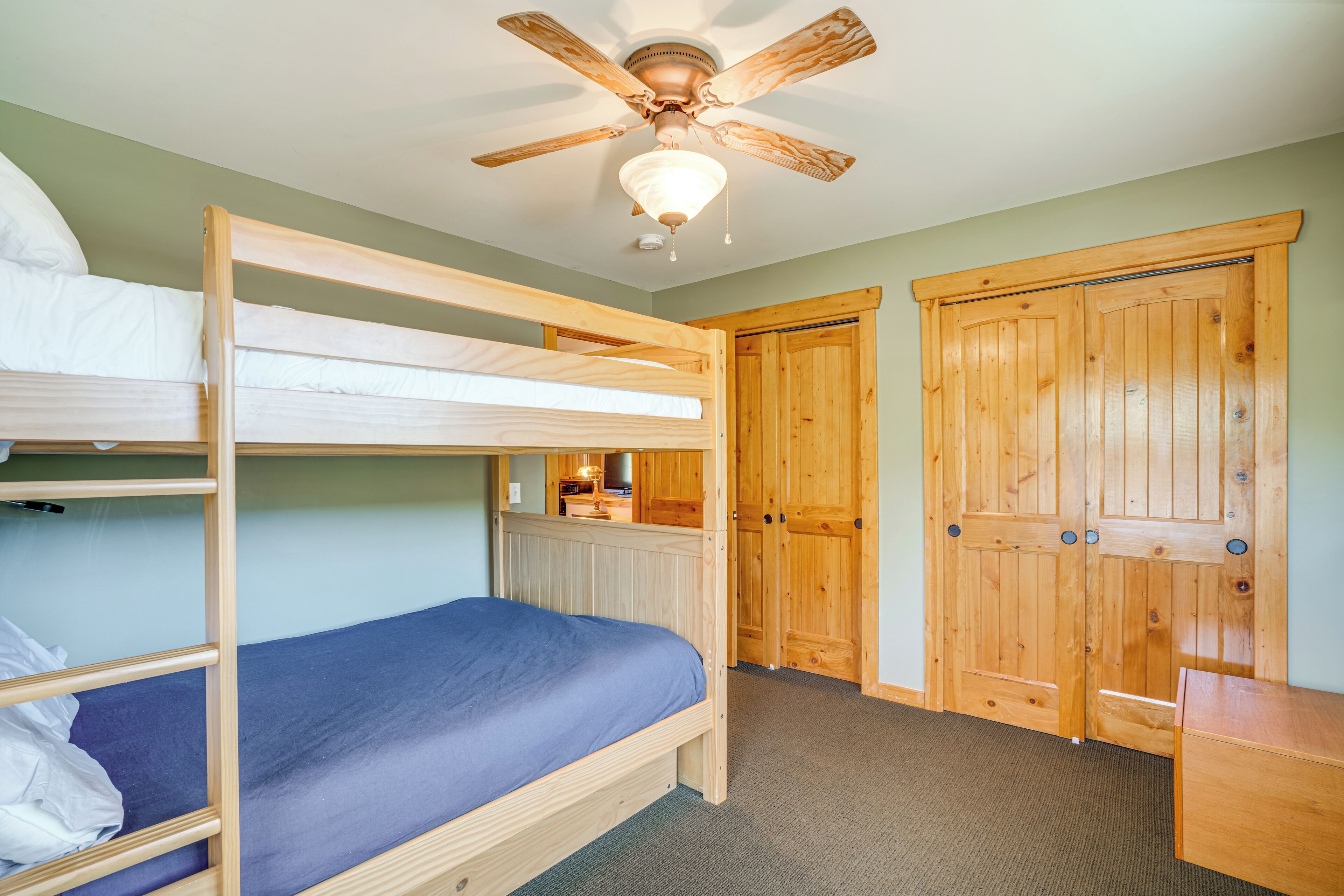A bunk bed room with a ceiling fan, wooden wardrobe, and a small desk.