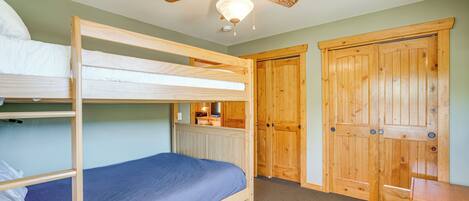 A bunk bed room with a ceiling fan, wooden wardrobe, and a small desk.