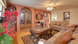 A living room with a brick fireplace, a wooden coffee table, and a beige sofa. - Hot Springs Home With Pool - 1/2 Mile to Oaklawn! (Hot Springs)