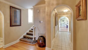 A hallway with a staircase, framed artwork, and a vase with sticks. - Hot Springs Home With Pool - 1/2 Mile to Oaklawn! (Hot Springs)