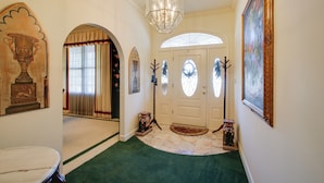 A hallway with a green carpet, a chandelier, a door with a glass panel, and a painting on the wall. - Hot Springs Home With Pool - 1/2 Mile to Oaklawn! (Hot Springs)