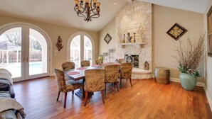 A dining area with a stone fireplace, wooden dining table, and chairs. - Hot Springs Home With Pool - 1/2 Mile to Oaklawn! (Hot Springs)