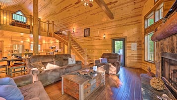 Un intérieur spacieux de chalet en bois, doté d’une cheminée, de canapés en cuir, d’un coin repas et d’un escalier menant à un niveau supérieur.