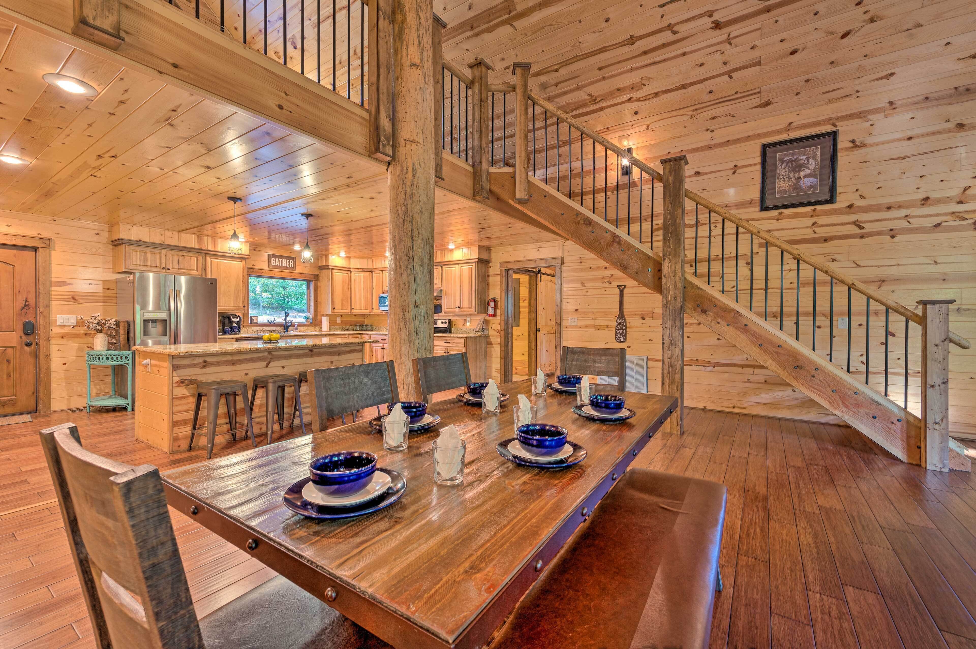 A spacious wooden cabin with a large dining table set for six, a kitchen area, and a staircase.