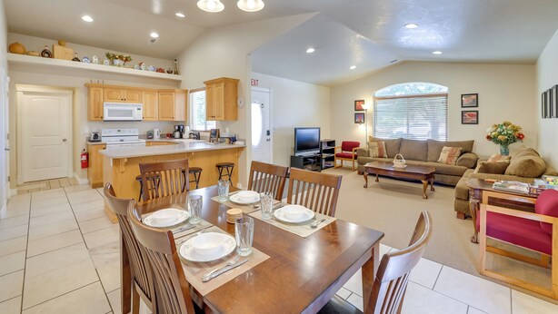 A spacious living area with a dining table set for four, a kitchen with wooden cabinets, a TV, and a comfortable seating area with a sofa and armchairs. - Family-friendly Utah Home, Easy Access to Zion! (La Verkin)