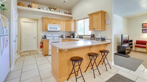 A modern kitchen with a central island, wooden cabinets, a microwave, and a television in the corner. - Family-friendly Utah Home, Easy Access to Zion! (La Verkin)