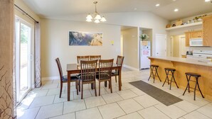 A dining area with a table and chairs, a kitchen with a counter and stools, and a large window with curtains. - Family-friendly Utah Home, Easy Access to Zion! (La Verkin)