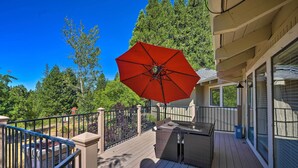 A wooden deck with outdoor furniture, a red umbrella, and a view of trees and a building. - Deck & Grill: Camino Home in Wine Country! (Camino)