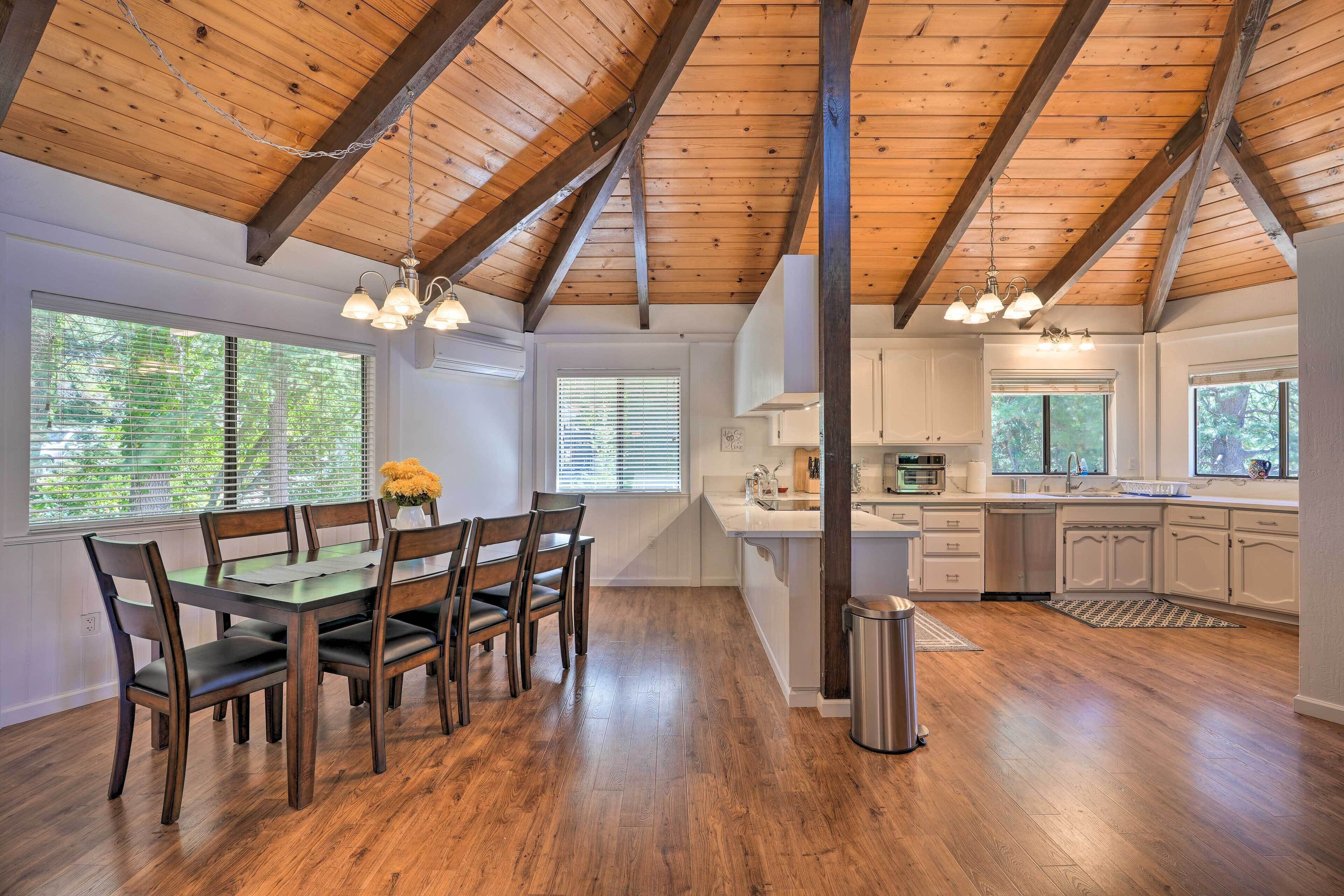 Una cocina amplia con vigas de madera, un comedor con mesa y sillas, y ventanas grandes.