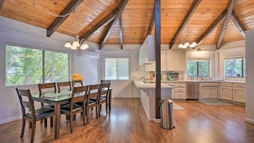 Una cocina amplia con vigas de madera, un comedor con mesa y sillas, y ventanas grandes.