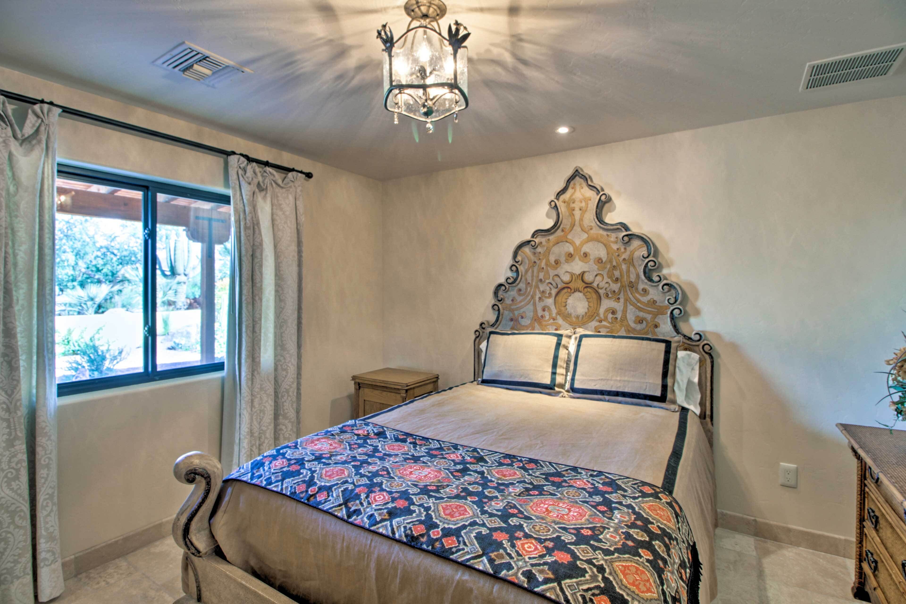 Un dormitorio con una cama grande, una araña, una ventana con cortinas y una mesita de noche pequeña.