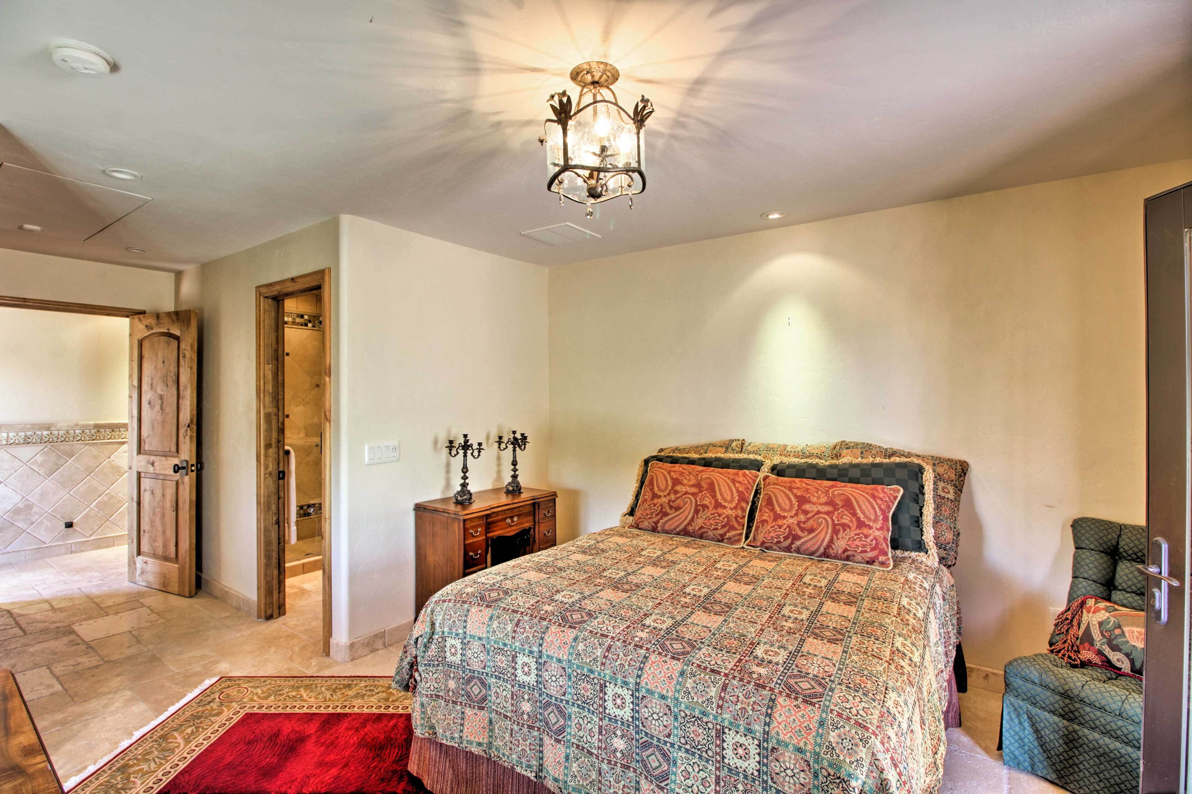 A bedroom with a large bed, a wooden door, a nightstand, and a chandelier.