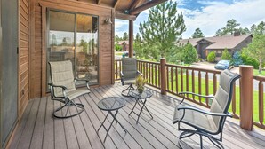 Une terrasse en bois avec des meubles d’extérieur, une porte vitrée donnant sur un espace abrité et une vue sur un quartier résidentiel.