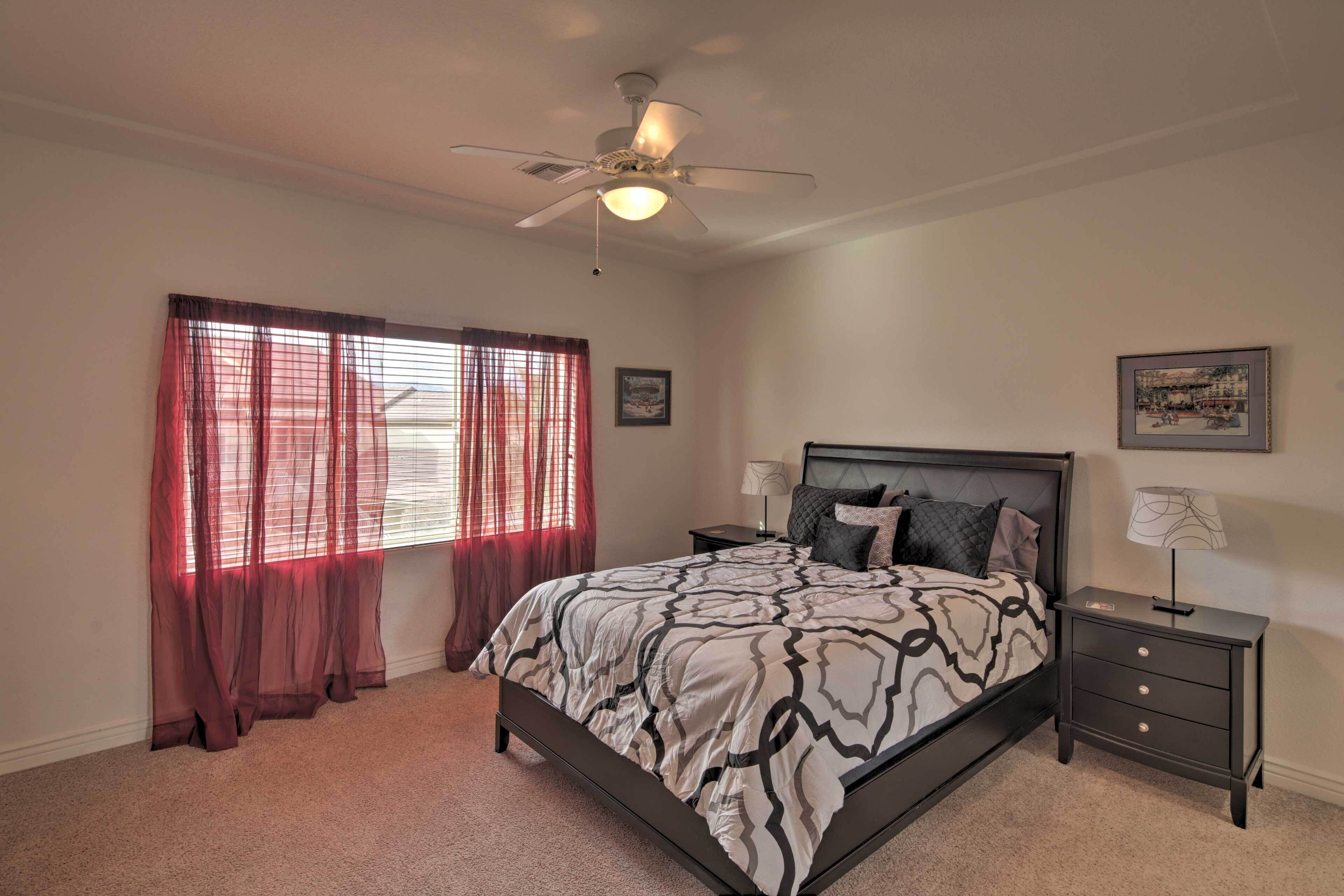 A bedroom with a bed, nightstands, a ceiling fan, and two wall-mounted lamps.