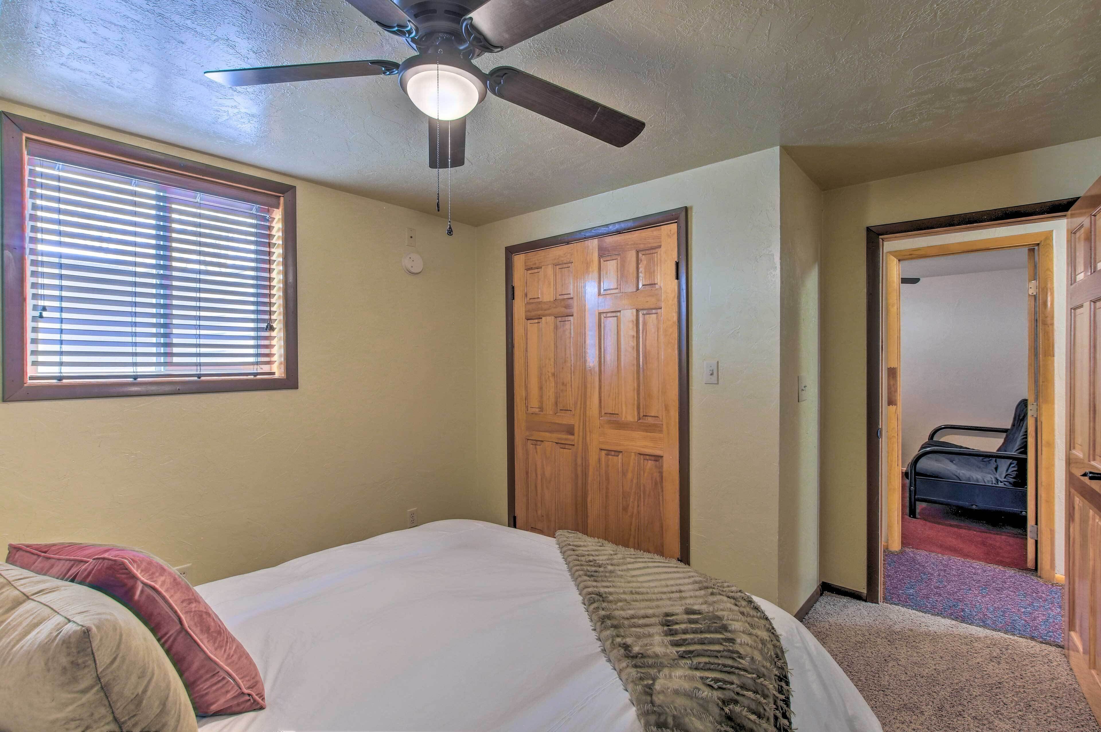 A bedroom with a bed, a ceiling fan, a wooden door, and a window with blinds.