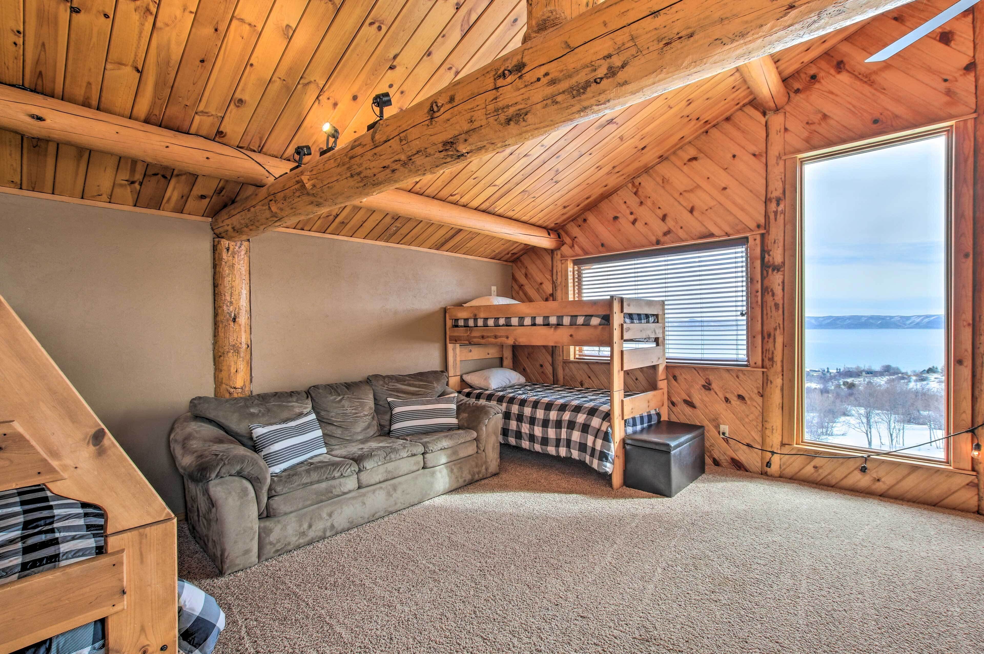 A cozy room with a bunk bed, a sofa, and a large window offering a view of the landscape.