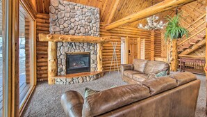 A log cabin interior with a stone fireplace, leather sofas, and a chandelier.