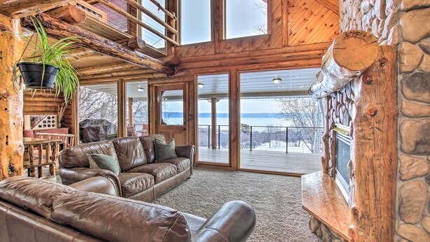 A cozy cabin interior with a leather sofa, a stone fireplace, and large windows offering a view of the outdoors.