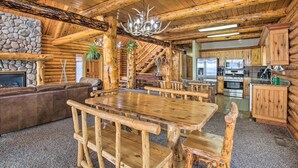 A rustic cabin interior with a stone fireplace, wooden dining table, and a kitchen area.