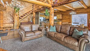 A log cabin interior with a leather sofa, wooden beams, and a kitchen area.