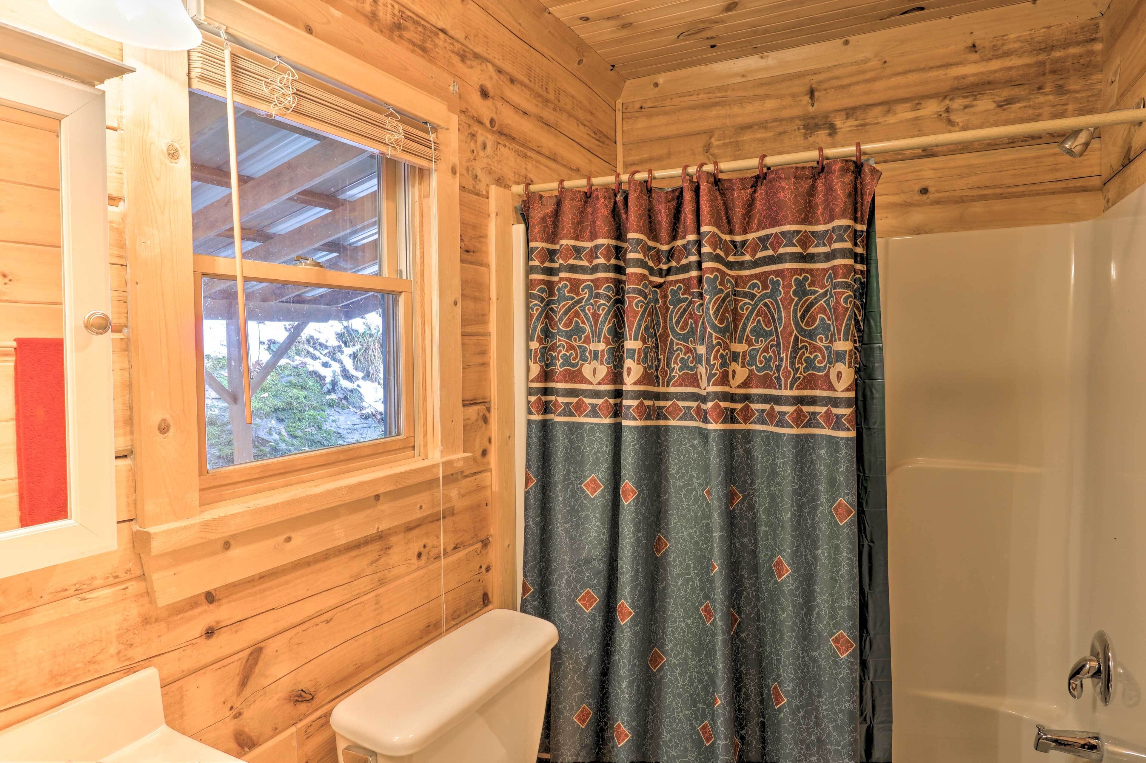 A wooden cabin bathroom with a window, a shower curtain, and a toilet.