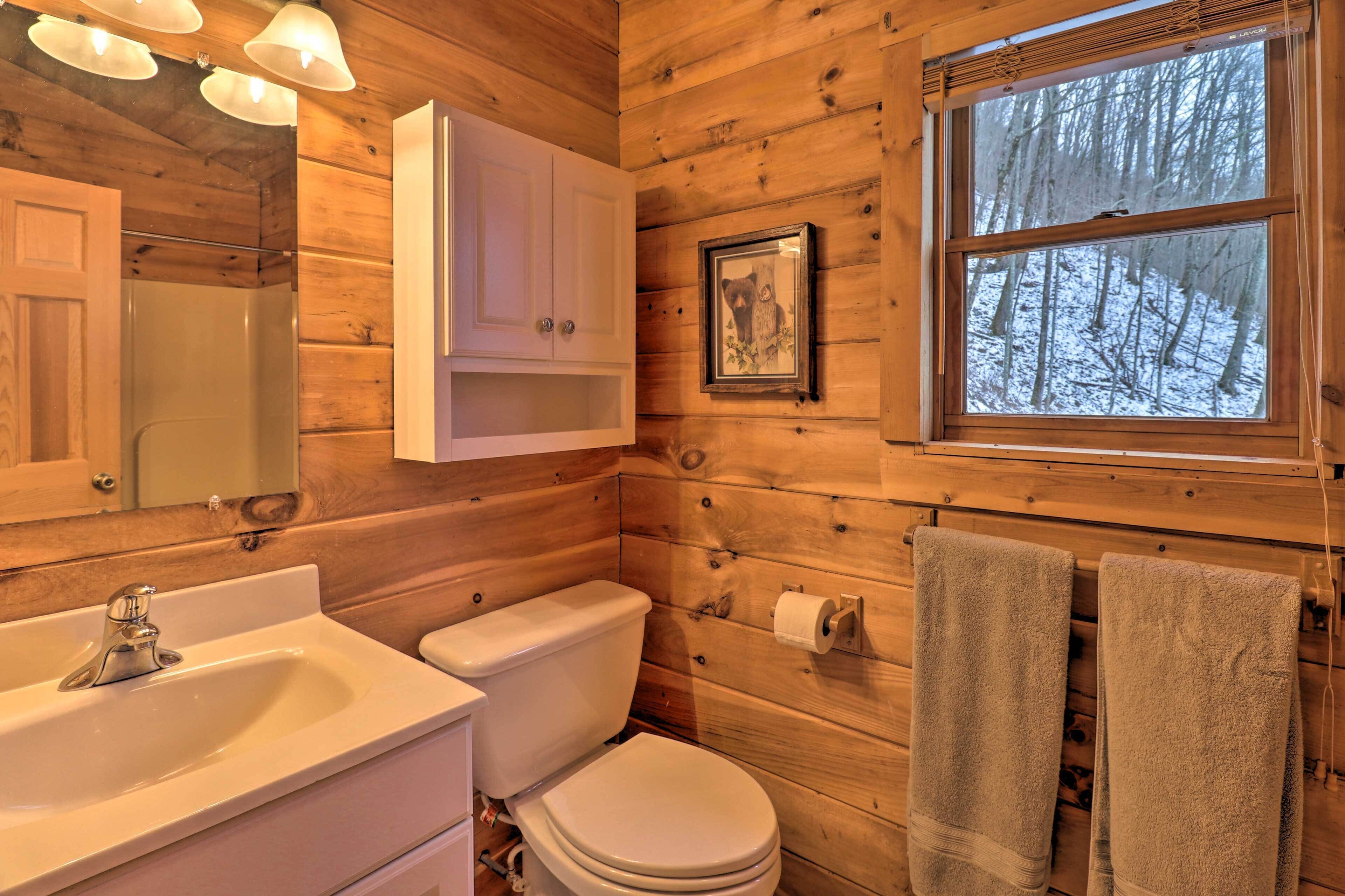 A wooden cabin bathroom with a sink, toilet, and a window with a snowy forest view.