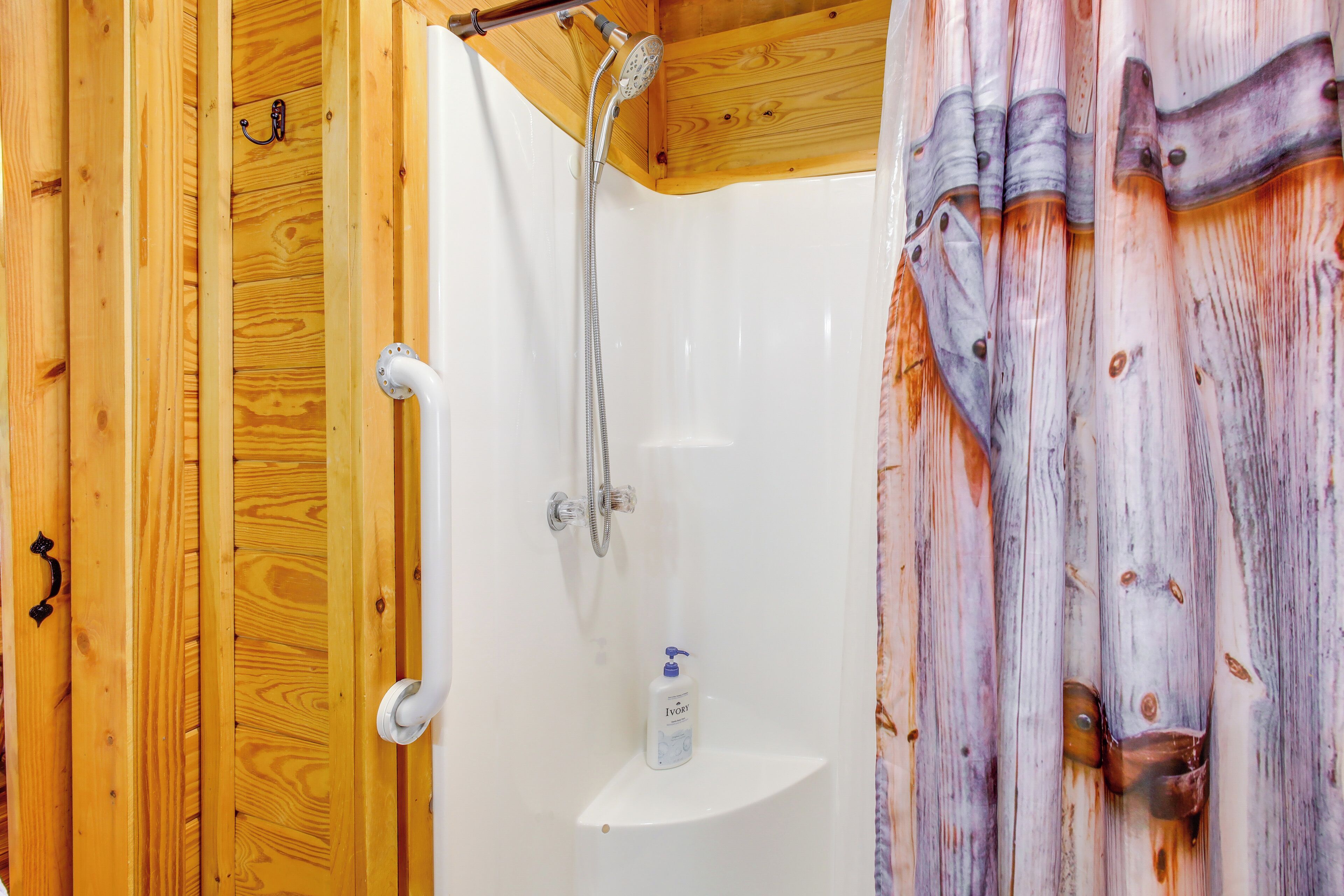 A wooden cabin bathroom with a shower, a white sink, and a soap dispenser.
