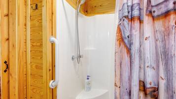 A wooden cabin bathroom with a shower, a white sink, and a soap dispenser.