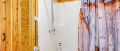 A wooden cabin bathroom with a shower, a white sink, and a soap dispenser.