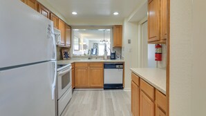 A kitchen with wooden cabinets, a white refrigerator, a dishwasher, and a coffee maker. - Central Cocoa Beach Condo w/ View, Steps to Beach! (Cocoa Beach)