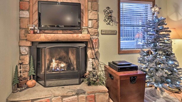 A cozy living room with a stone fireplace, a television on a wooden shelf, a Christmas tree, and a 'WELCOME' sign. - Cozy Angel Fire Condo < Half Mi to Resort! (Angel Fire)