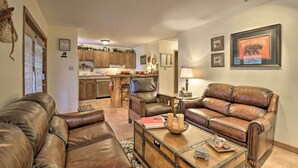 A living room with leather sofas, a coffee table, and a kitchen in the background. - Cozy Angel Fire Condo < Half Mi to Resort! (Angel Fire)