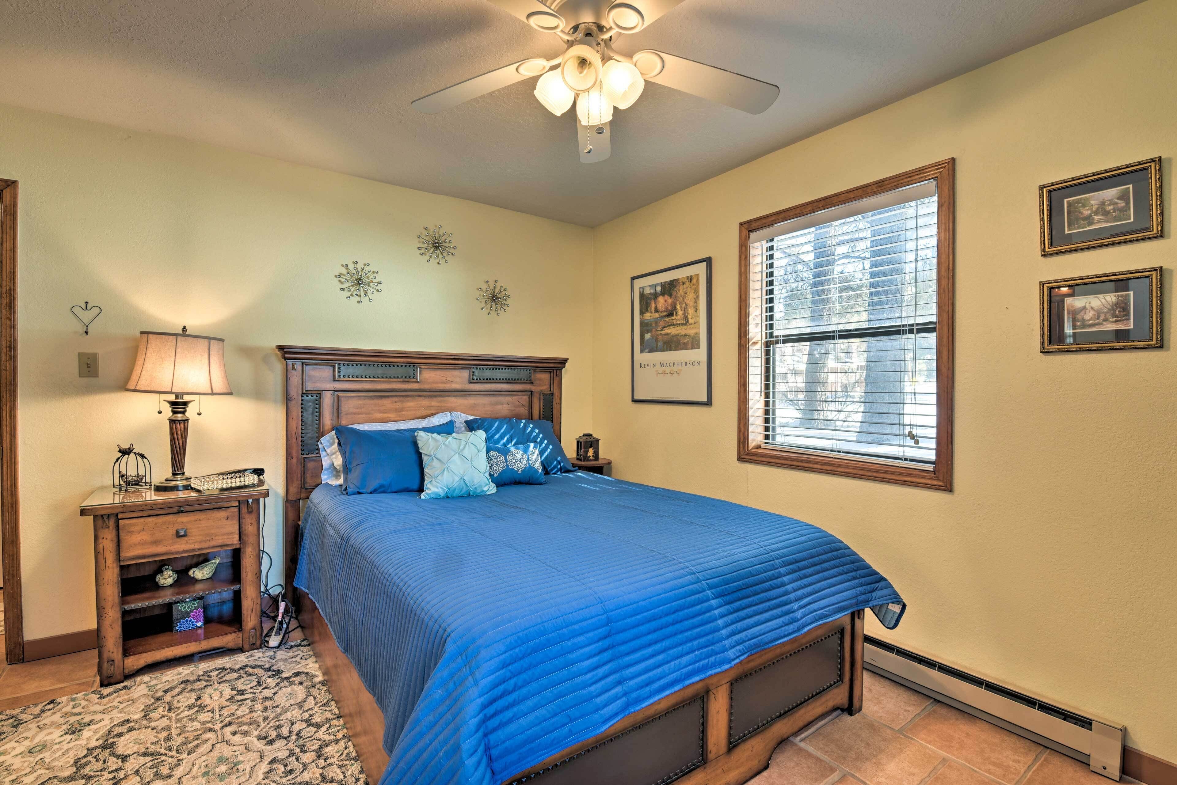 A bedroom with a bed, a nightstand, a lamp, a ceiling fan, and a window with blinds.