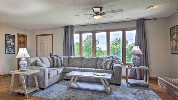 A living room with a sectional sofa, a coffee table, two side tables with lamps, a ceiling fan, and large windows with curtains. - 'blue Moon Cottage' w/ Amazing Views of 5 Counties (Danville)