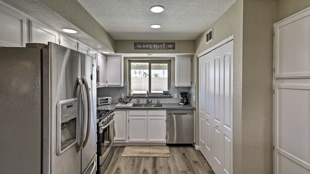 A kitchen with white cabinets, stainless steel appliances, and a window with a view of palm trees. - Near Marina: Home w/ Pool & Views in Lake Havasu! (Lake Havasu City)