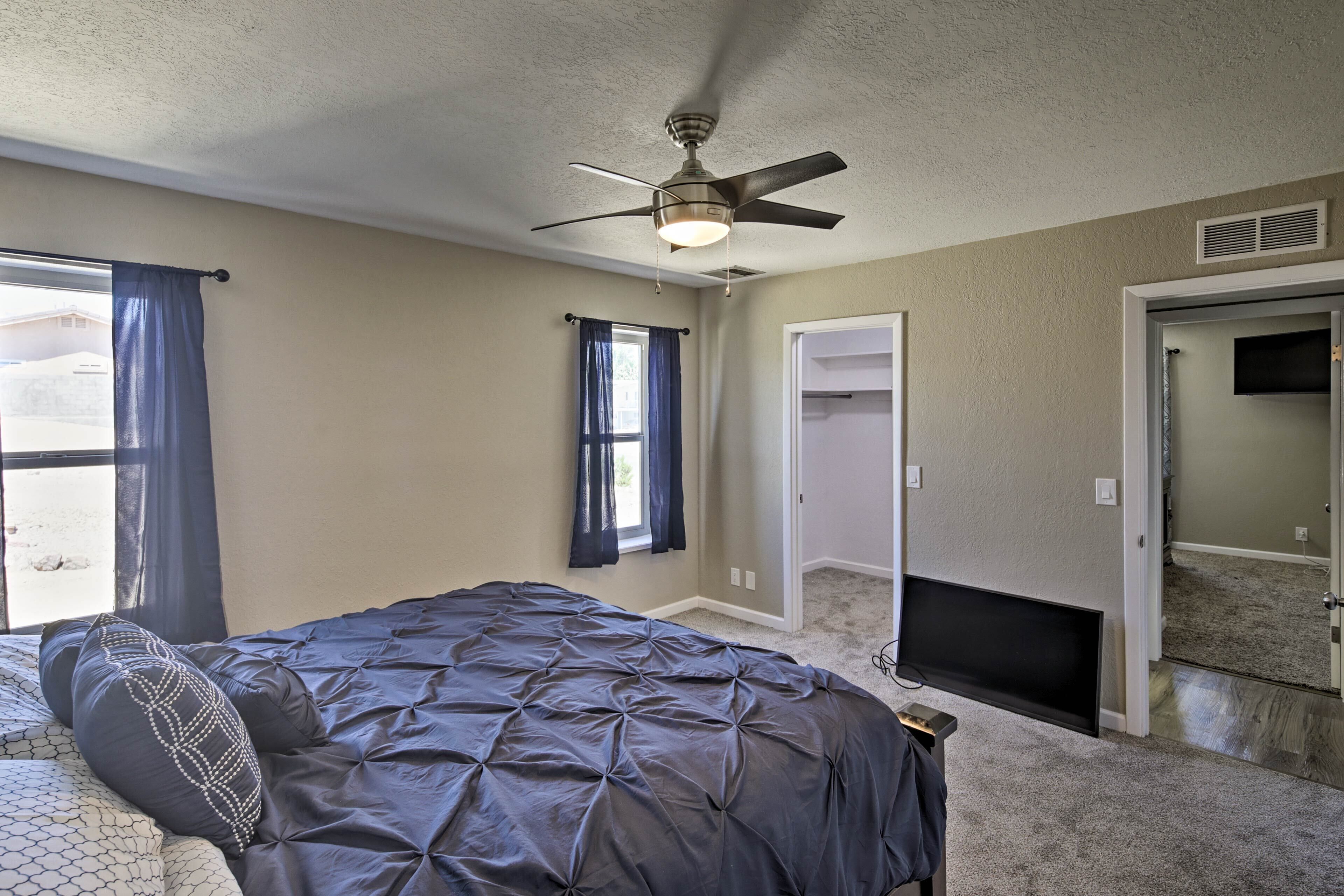 Une chambre à coucher avec un lit, un ventilateur de plafond et un téléviseur fixé au mur.
