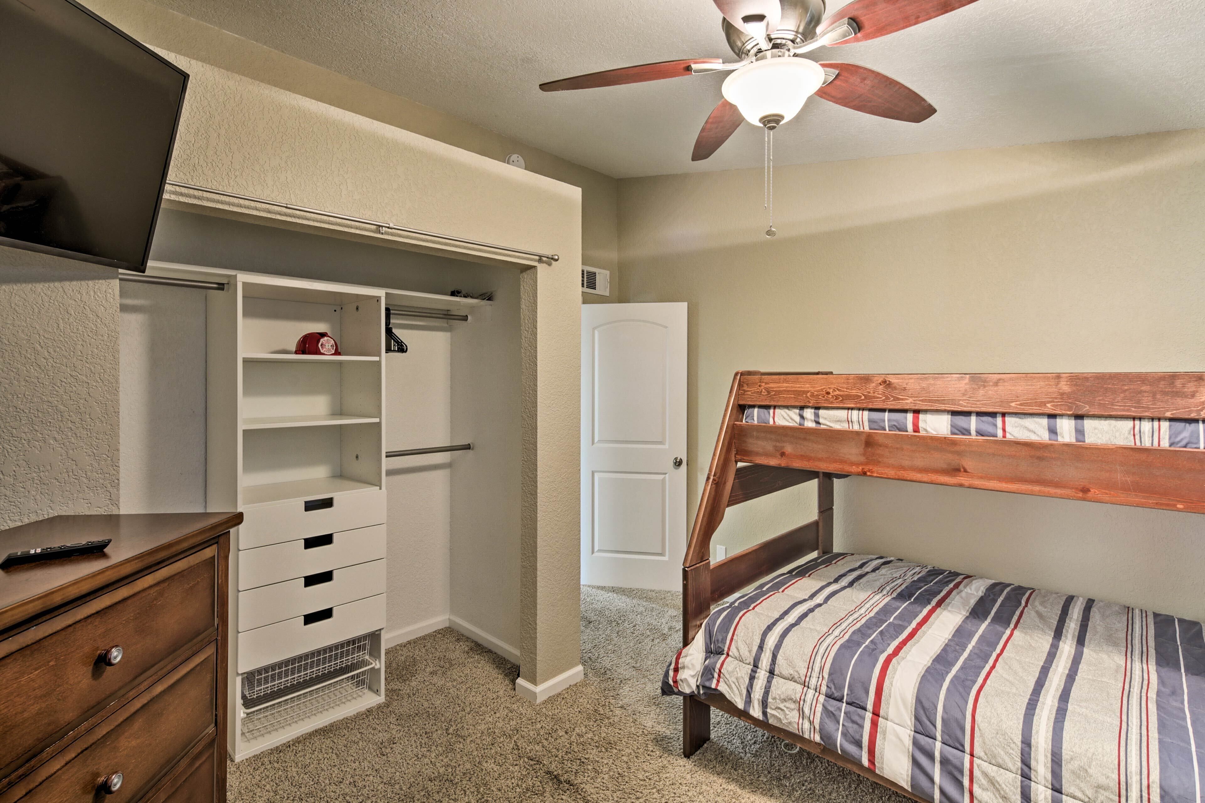 Ein Schlafzimmer mit Etagenbett, Kleiderschrank, Deckenventilator und Schreibtisch mit Schubladen.