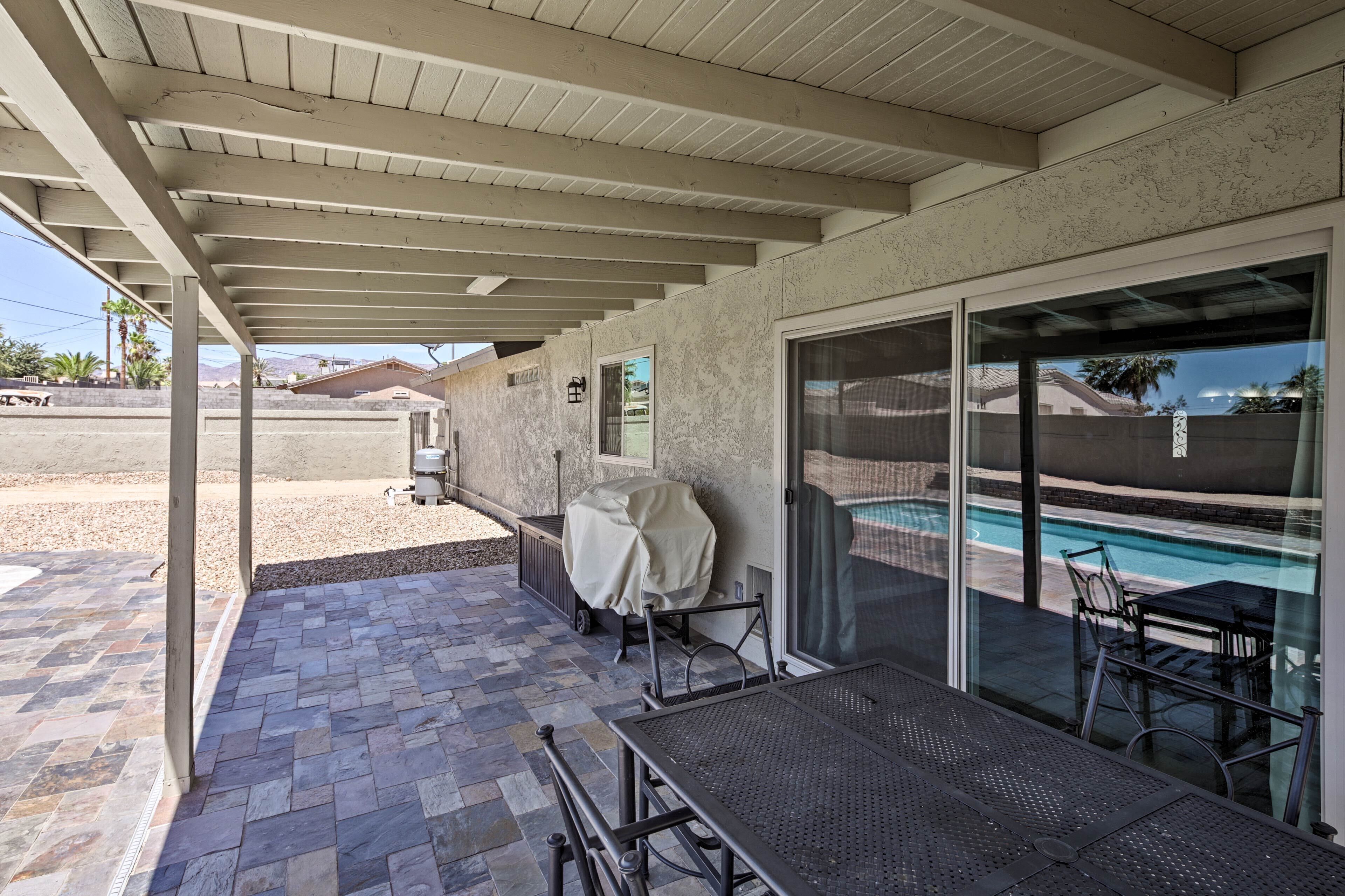 Un patio cubierto con piscina, mobiliario exterior y zona de parrilla techada.