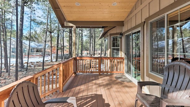 Eine Holzterrasse mit zwei Adirondack-Stühlen und einem Tisch, mit Blick auf eine bewaldete Gegend.