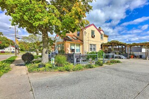 A two-story house with a red roof, a front porch, and a garden area with plants and a small tree. - Cincinnati Basement Unit ~ 10 Mi to Downtown! (Cincinnati)