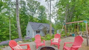 Uma cabana rústica com lareira e cadeiras Adirondack vermelhas em meio a uma área arborizada.