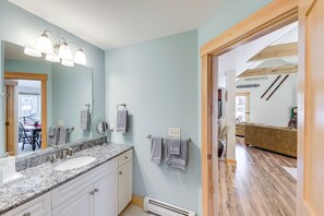 A bathroom with a double sink, vanity, and a mirror. There are towels hanging on the wall and a heater on the floor.