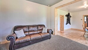Un salon spacieux avec un canapé en cuir marron, une porte en bois et une grande poutre en bois au plafond.