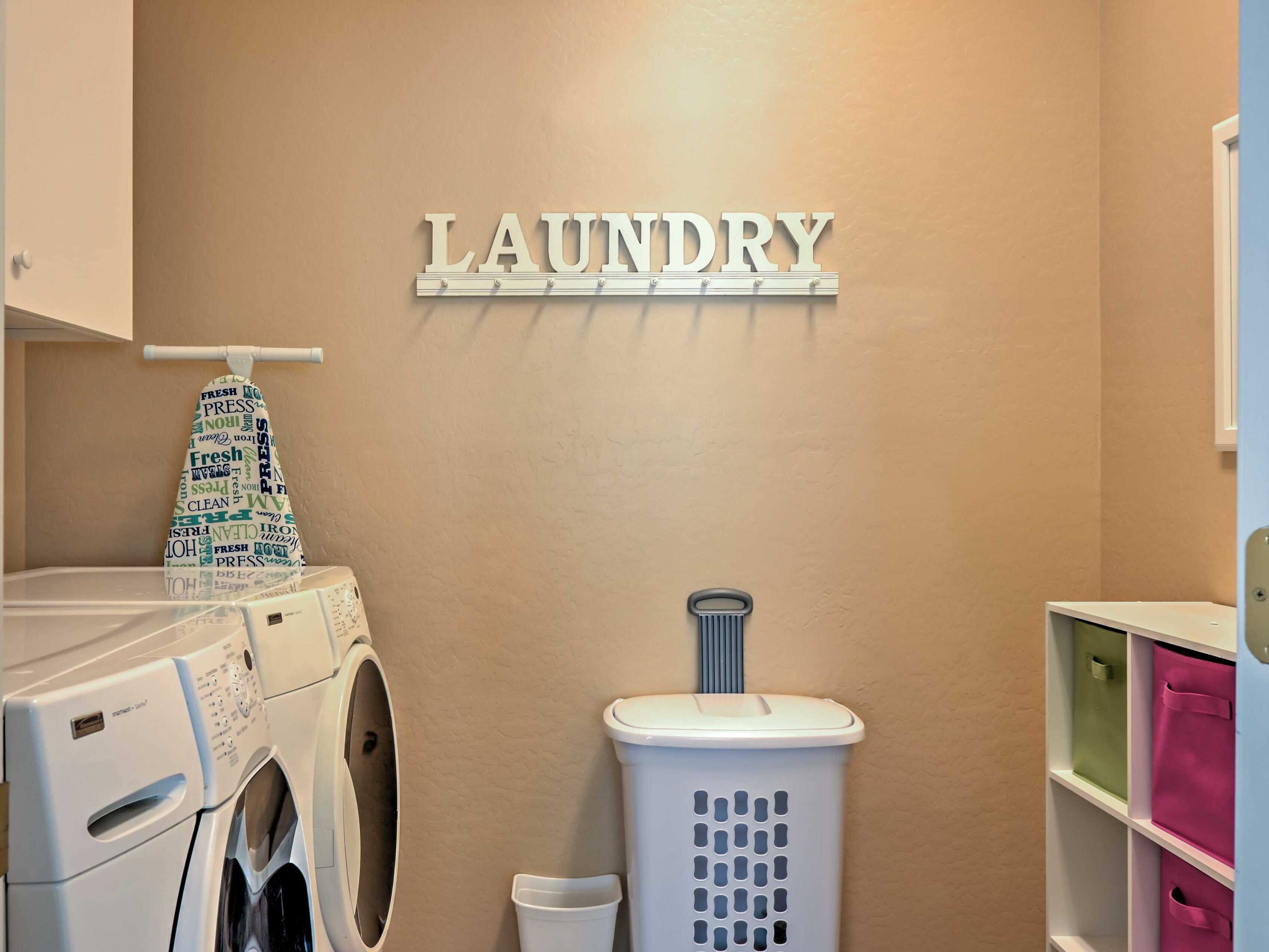 A laundry area with a wall-mounted sign reading "LAUNDRY," a washing machine, a drying rack, a laundry basket, and storage shelves.