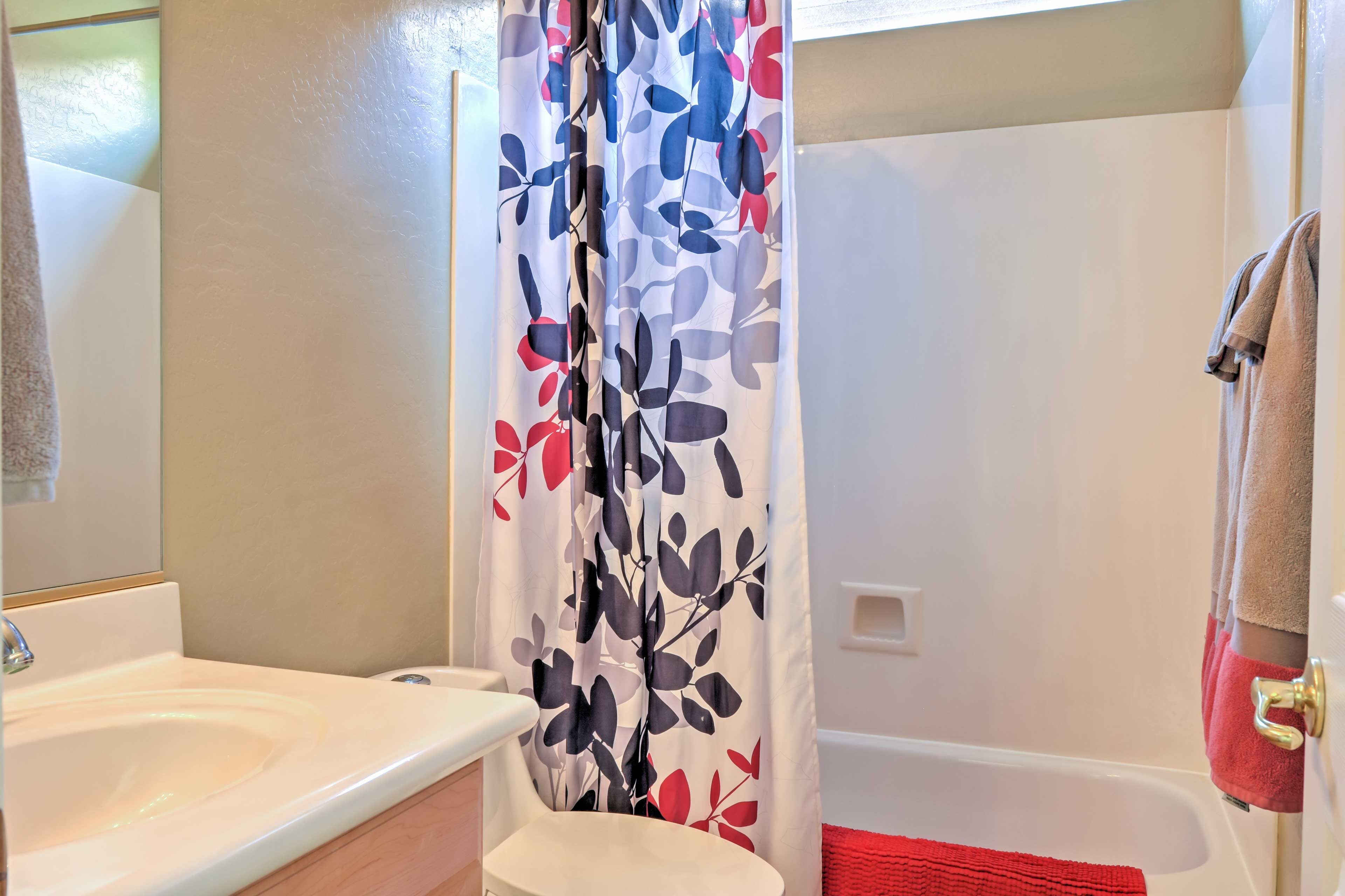 A bathroom with a white sink, a shower curtain with a floral pattern, and a red bath mat.