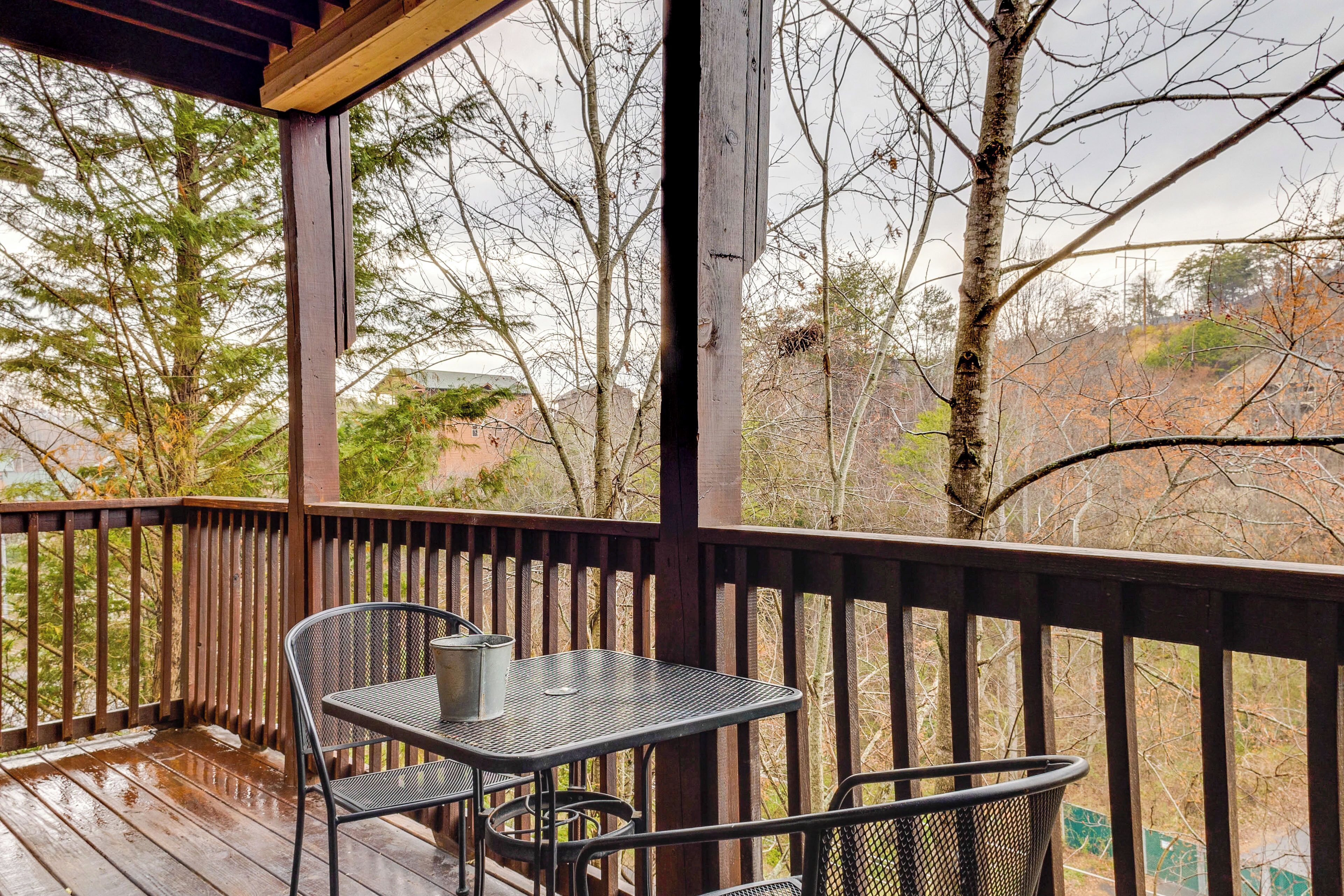 A wooden deck with a metal table and chairs, overlooking a forested area.